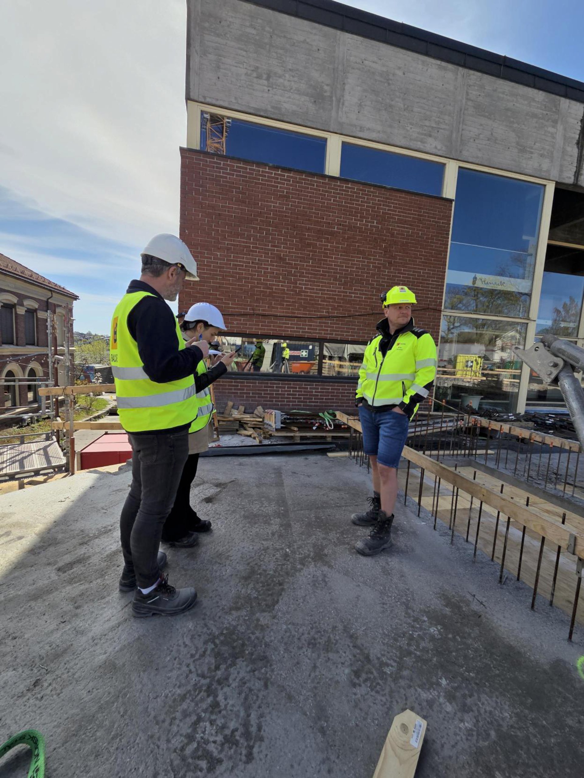 Utendørs på byggeplassen. Tre mennesker i refleksvester snakker sammen. Intervjusituasjon.